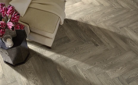 Herringbone hardwood floor with beige chair, flowers in vase 