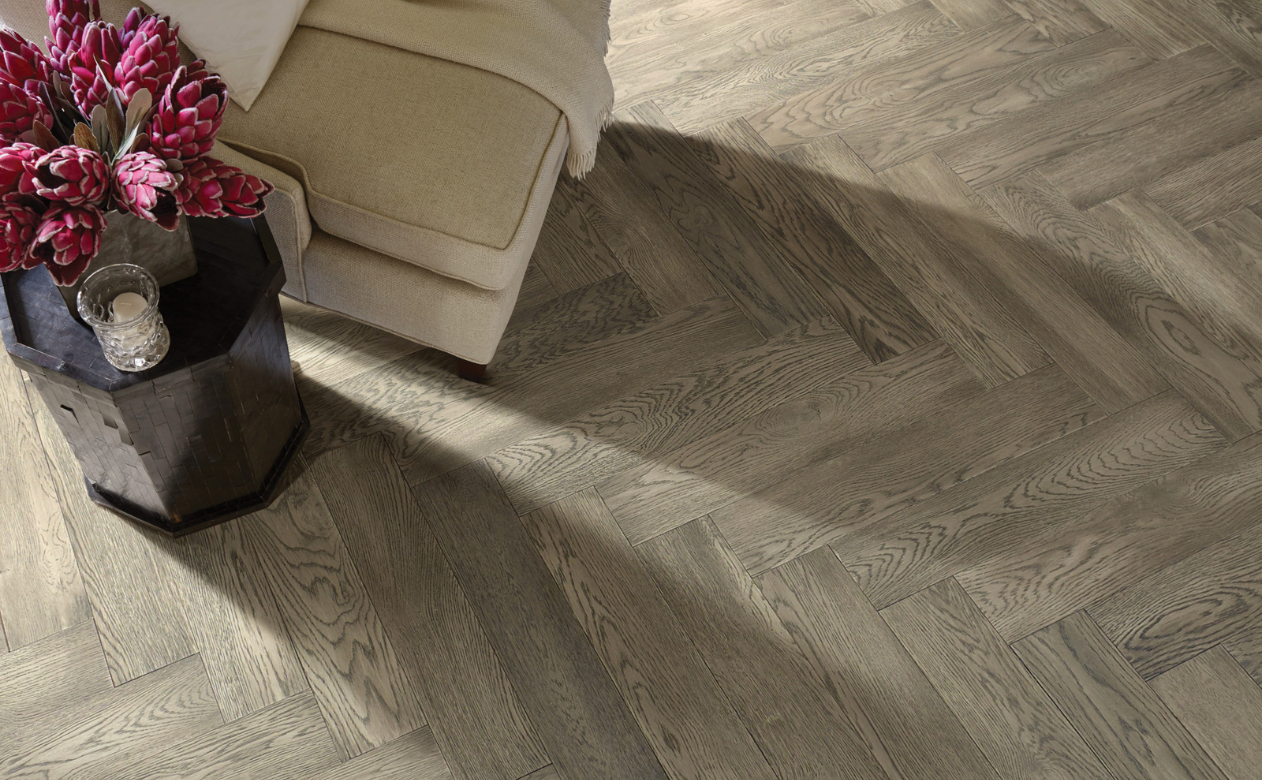 Herringbone hardwood floor with beige chair, flowers in vase 